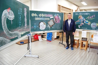 自作の黒板アートを前に話す峰崎国夫さん＝大久保北コミセン