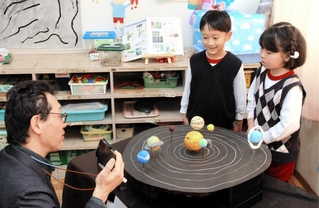 井上毅館長（左）に太陽系惑星の模型について説明する園児ら＝播陽幼稚園