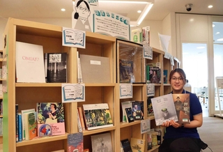 司書らの「推し」が並ぶ本棚で、大人向けの絵本を手にする嶋田楓さん＝あかし市民図書館