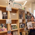 司書らの「推し」が並ぶ本棚で、大人向けの絵本を手にする嶋田楓さん＝あかし市民図書館