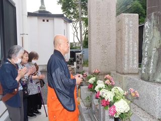 犠牲者の墓の前で読経を上げる松尾義康住職（右）と、手を合わせる参列者＝明石市上ノ丸１