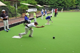 人工芝が敷かれたローンボウルズのコートで狙いを定めて球を投げる選手＝県立明石公園
