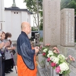犠牲者の墓の前で読経を上げる松尾義康住職（右）と、手を合わせる参列者＝明石市上ノ丸１