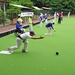 人工芝が敷かれたローンボウルズのコートで狙いを定めて球を投げる選手＝県立明石公園