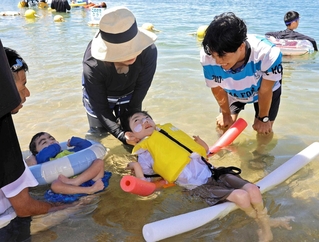体を支えてもらって海水浴を楽しむ参加者＝大蔵海岸海水浴場