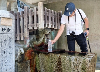亀の口から湧き出る「亀の水」をくむ人。傍らに永井荷風の文学碑が立つ＝明石市人丸町