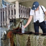 亀の口から湧き出る「亀の水」をくむ人。傍らに永井荷風の文学碑が立つ＝明石市人丸町