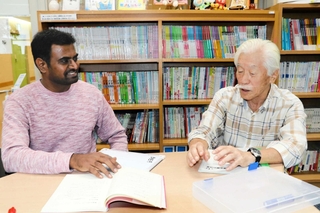 ボランティアの中村英夫さん（右）からレッスンを受けるシング・サントシュ・べニュゴパルさん＝明石市東仲ノ町