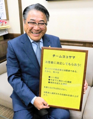 企業理念「チームヨコヤマ」を手に笑顔の井上雅文社長＝明石市相生町２