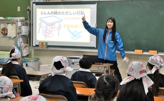 手拭いの頭巾をかぶった児童らに、地震の揺れから身を守る方法を伝える日工の日野桃子さん＝江井島小学校