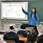 手拭いの頭巾をかぶった児童らに、地震の揺れから身を守る方法を伝える日工の日野桃子さん＝江井島小学校