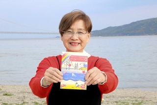 清掃活動を続ける望海浜で、２冊目の著書を手にする藤本真知子さん＝明石市船上町
