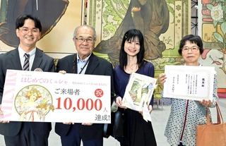 来場者１万人達成の記念撮影に応じる（右から）遠藤文子さん、由加里さん親子と尾形寿行さんら＝明石市立文化博物館