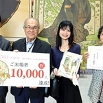 来場者１万人達成の記念撮影に応じる（右から）遠藤文子さん、由加里さん親子と尾形寿行さんら＝明石市立文化博物館