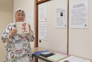生沼勝氏に関する資料が並ぶコーナーで河井省三氏の著作を手に持つ足羽静さん＝明石市明南町２