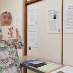 生沼勝氏に関する資料が並ぶコーナーで河井省三氏の著作を手に持つ足羽静さん＝明石市明南町２