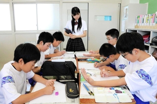 明石高校生の指導で自分の手を写生する子どもたち＝人丸小学校
