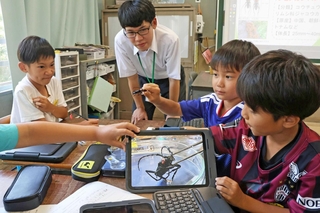 高校生の指導でクビアカツヤカミキリの標本を観察する児童ら＝高丘東小学校