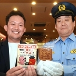 ぱっすーの玉子せんべいを手にする足立雅樹署長（右）と永楽堂の永井健太副社長＝明石市本町１