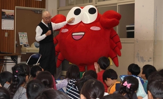 わさカーニの着ぐるみとともに児童らの質問に答える入江俊勝さん＝明石市和坂２