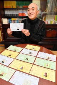 過去１２年の受験票を前に、目標達成を誓う土井章光さん＝淡路市