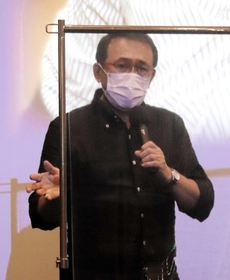 舞台あいさつで、コロナ感染防止の透明板越しに話す長尾和宏医師＝洲本オリオン