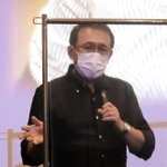 舞台あいさつで、コロナ感染防止の透明板越しに話す長尾和宏医師＝洲本オリオン