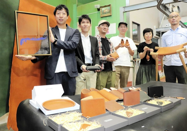 淡路島レザーのロゴを示す高原さん（左端）と、商品を持つ革作家ら＝淡路市塩田新島