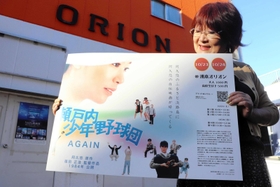 洲本オリオンの前で瀬戸内少年野球団のポスターを持つ山中さん＝洲本市本町５