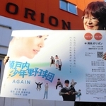 洲本オリオンの前で瀬戸内少年野球団のポスターを持つ山中さん＝洲本市本町５