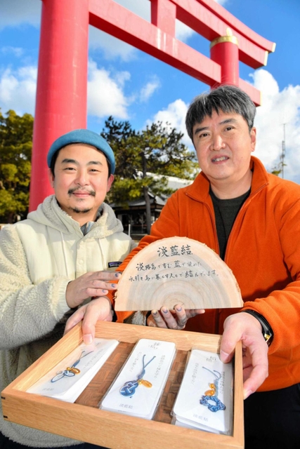 完成した藍染めのお守りを持つ根岸誠一さん（左）と、森の木ファームの生活支援員柳尚孝さん＝おのころ島神社