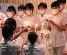 ナイチンゲール像にともした火を自分のろうそくに移す学生＝平成淡路看護専門学校