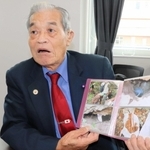 パラオで遺骨収集に参加した時の写真を手に、父の戦死などについて話す谷忠義さん＝淡路市役所