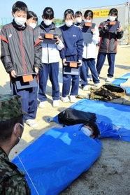 ブルーシートの両端を固定した簡易寝袋を体験する生徒＝南淡中学校