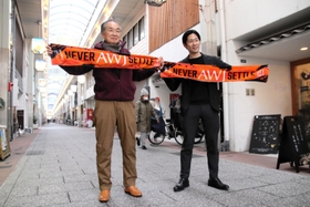 アーケードでＦＣ．ＡＷＪのスポーツタオルを広げる本町五六商店街協同組合の山本理事長（左）とＡＷＪの片山代表＝洲本市本町５