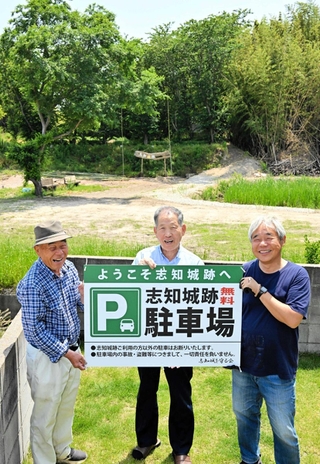 志知城跡（後方）の駐車場として自宅前のスペースを提供した藤江武弘さん（中央）ら＝南あわじ市志知