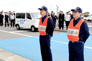 出発式で多くの職員に見守られる佐竹史憲主事（左）と山名伸和係長＝淡路市生穂新島