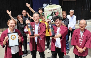 世界一の酒に選ばれた都美人の純米吟醸「太陽」と喜ぶ社員ら＝南あわじ市榎列西川