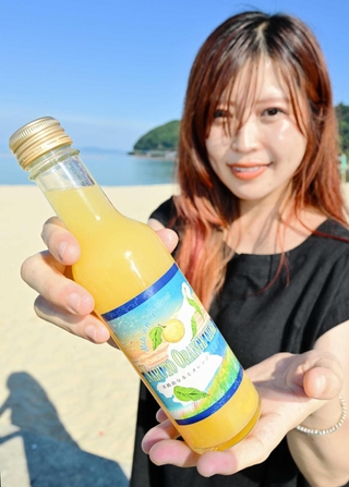 なるとオレンジサイダーをＰＲする増田薫さん＝洲本市の大浜海岸