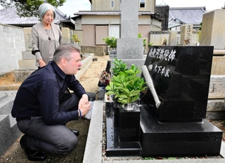 久下本誠吾さんの墓前で涙ぐむブライアン・アームストロングさん。後方は久下本さんの妻滋子さん＝浄光寺