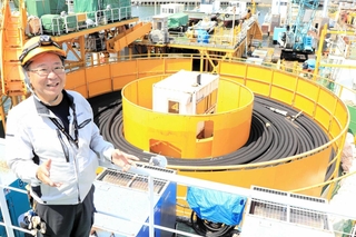 既存の台船で海底ケーブルを巻いたターンテーブルを背に語る関勝社長＝淡路市生穂新島