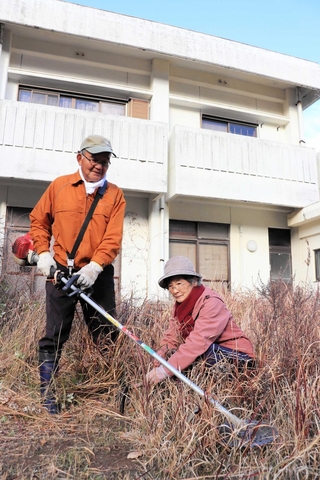 今も残る鉄筋の家の前で、伸びた雑草を刈り取る田中益也さん（左）、千鶴子さん＝淡路市野島蟇浦