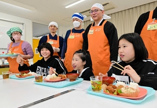 子ども食堂を再開した「ボランティアみらい」のメンバーと食事を味わう子どもたち＝志筑小学校