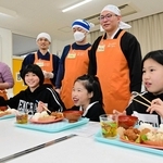 子ども食堂を再開した「ボランティアみらい」のメンバーと食事を味わう子どもたち＝志筑小学校