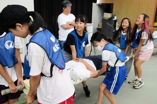竹の棒と毛布で作った担架で人を運ぶ児童ら＝南あわじ市役所