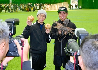 スポーツ紙のリクエストに応え、淡路島特産のタマネギと干しダコを手にする近本光司選手（左）と村上頌樹投手＝淡路佐野運動公園