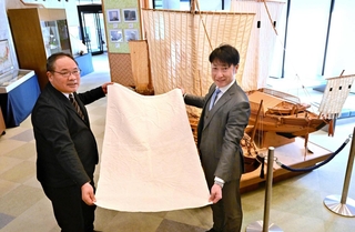 再現した松右衛門帆のタペストリーを手にする洲本市の浜辺学副市長（左）と高砂市観光交流ビューローの新井誠三理事長＝高田屋嘉兵衛公園