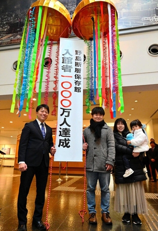 くす玉を割って入館１千万人達成を祝う荒川裕也さん一家（右）と戸田敦大市長＝淡路市小倉
