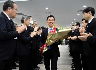 花束を受け取り、職員らに拍手で迎えられる吉平敏孝市長＝洲本市役所