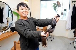 ヘアドネーションのためカットした約５０センチの髪の毛を手に「伸ばしてきて良かった」と笑顔を見せる東原祥真さん＝洲本市池内
